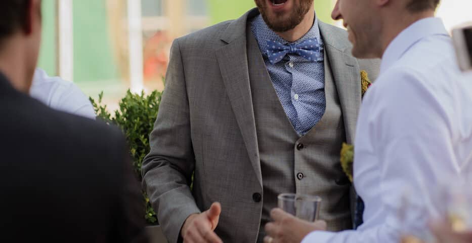 A man in a gray suit laughing and enjoying a conversation with others at an outdoor gathering.