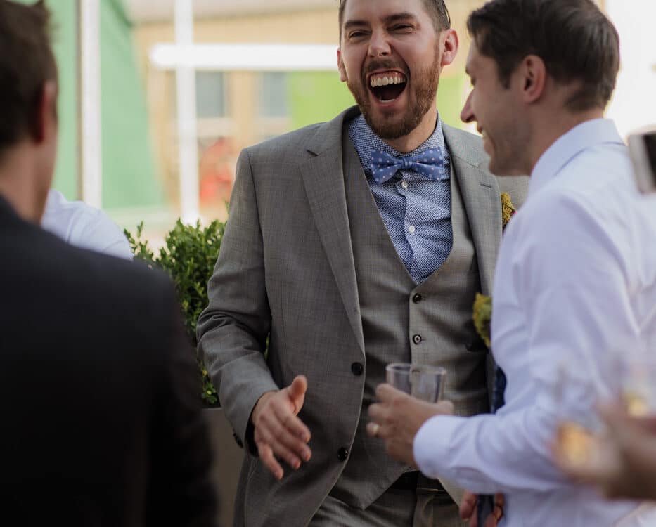A man in a gray suit laughing and enjoying a conversation with others at an outdoor gathering.