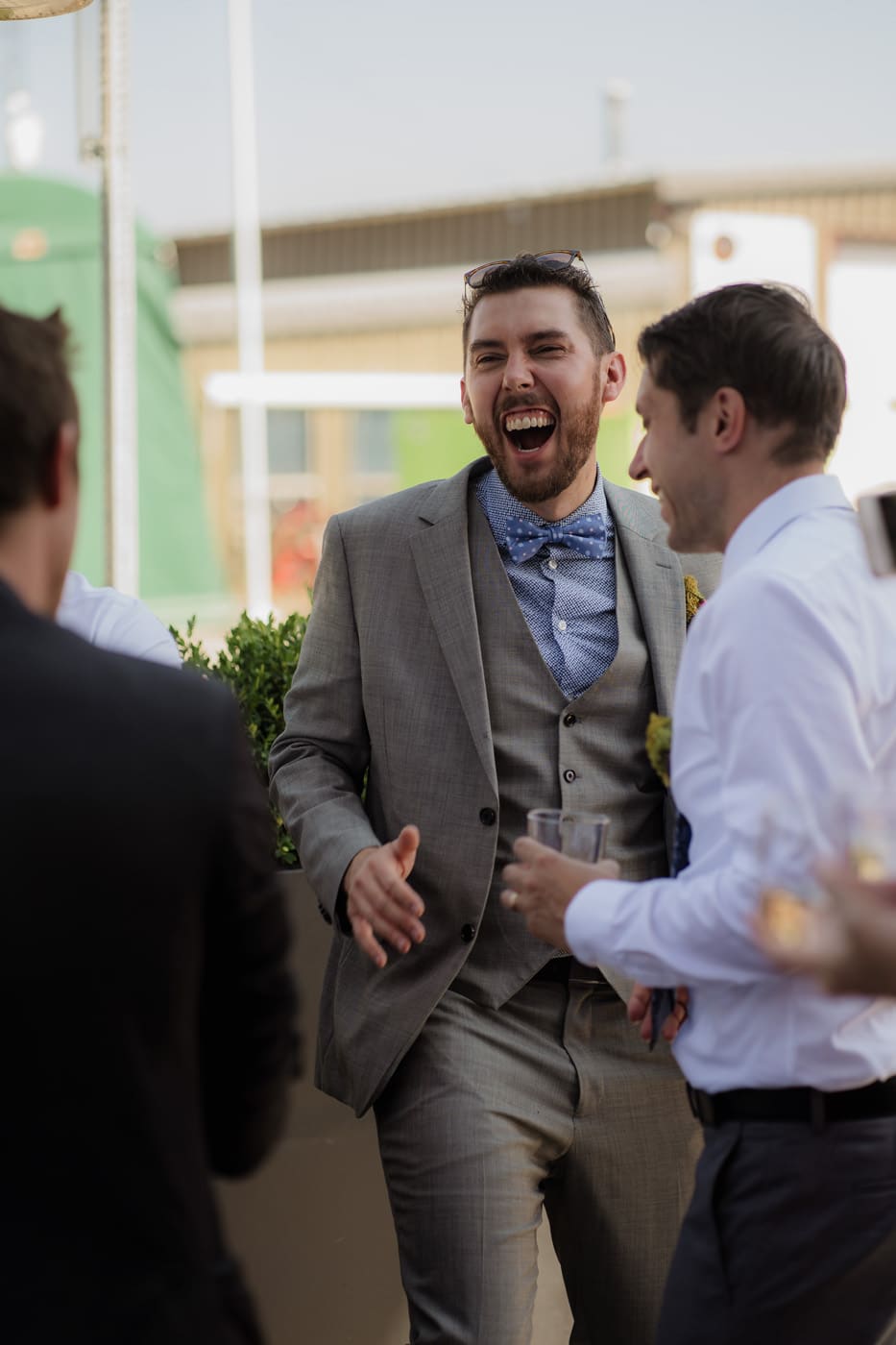 A man in a gray suit laughing and enjoying a conversation with others at an outdoor gathering.