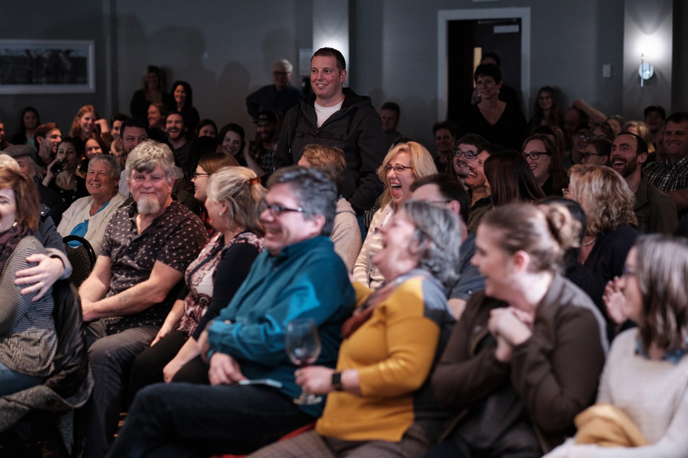 A crowd of people laughing and enjoying an event, with one man standing in the foreground.