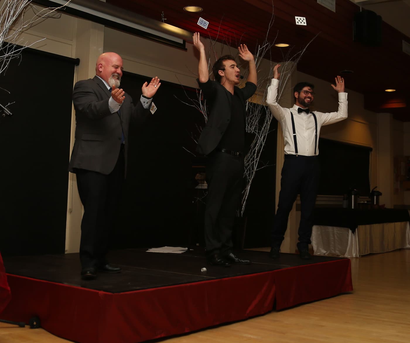 Three men on stage with raised hands, performing in a festive setting.