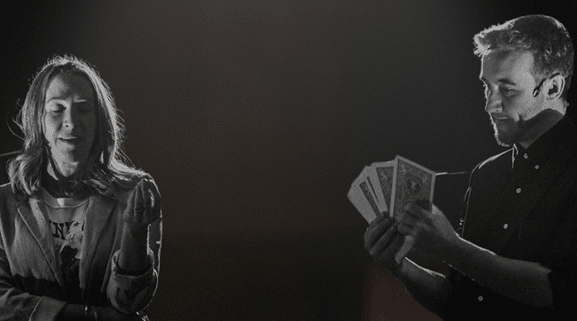 A woman appears to be in disbelief or shock, while a man stands beside her holding multiple dollar bills, suggesting a dramatic or magical moment.