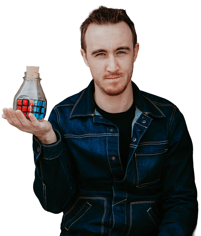 A person holding a glass container with a Rubik's Cube inside, wearing a denim jacket.
