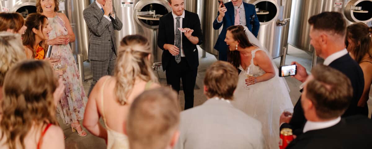 A group of people at a wedding, gathered around a card trick performer.