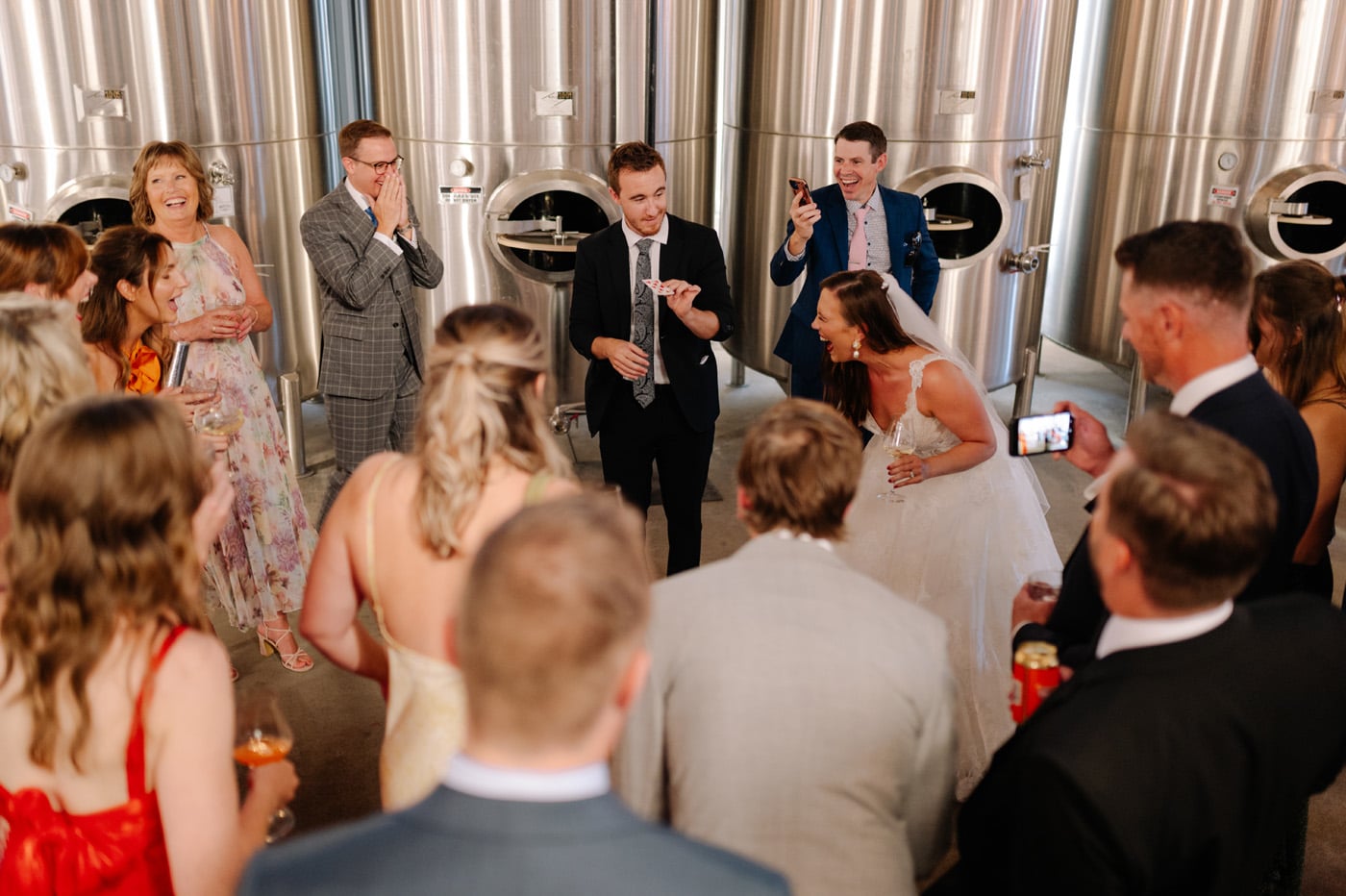 A group of people at a wedding, gathered around a card trick performer.