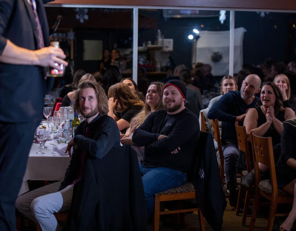 A magician performing for an audience at an event, with guests reacting with laughter and surprise.
