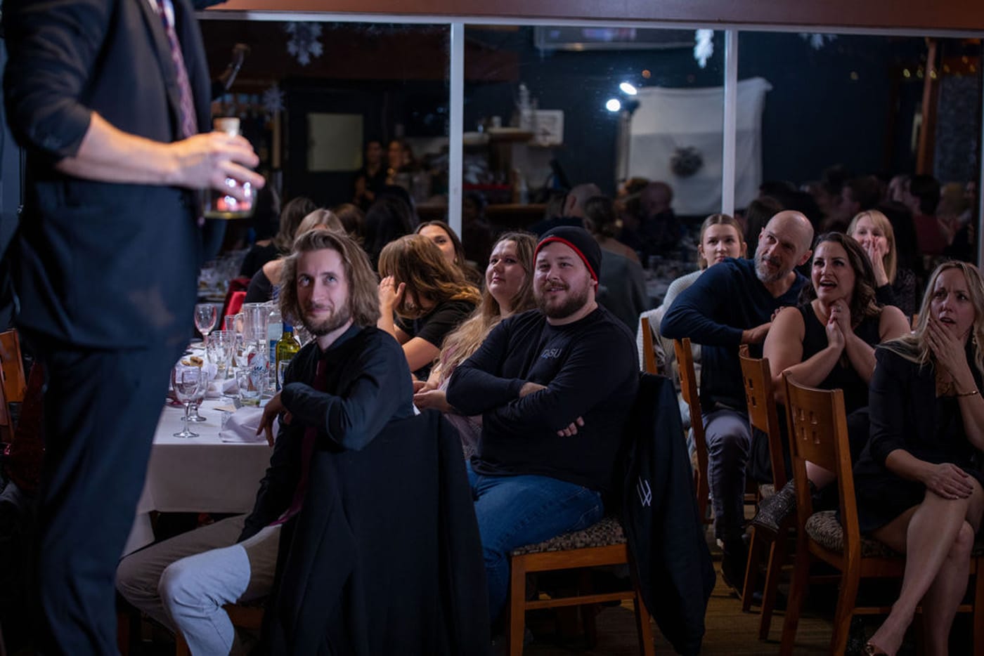 A magician performing for an audience at an event, with guests reacting with laughter and surprise.