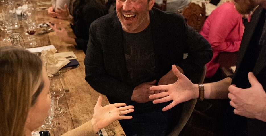 A group of people enjoying a lively conversation at a dinner table, with one person laughing and engaging animatedly with another.