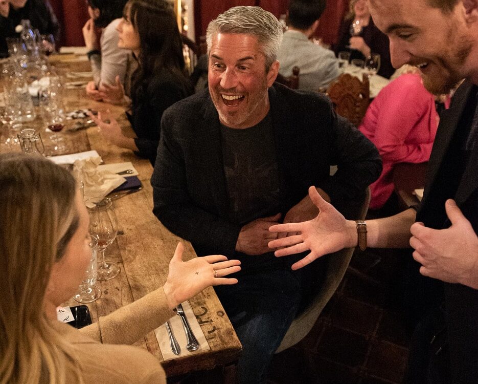 A group of people enjoying a lively conversation at a dinner table, with one person laughing and engaging animatedly with another.