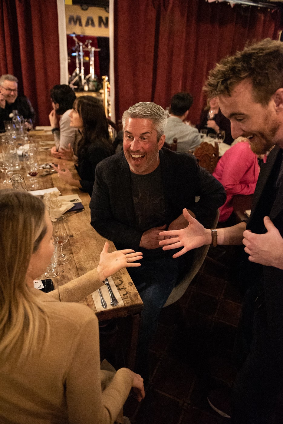A group of people enjoying a lively conversation at a dinner table, with one person laughing and engaging animatedly with another.
