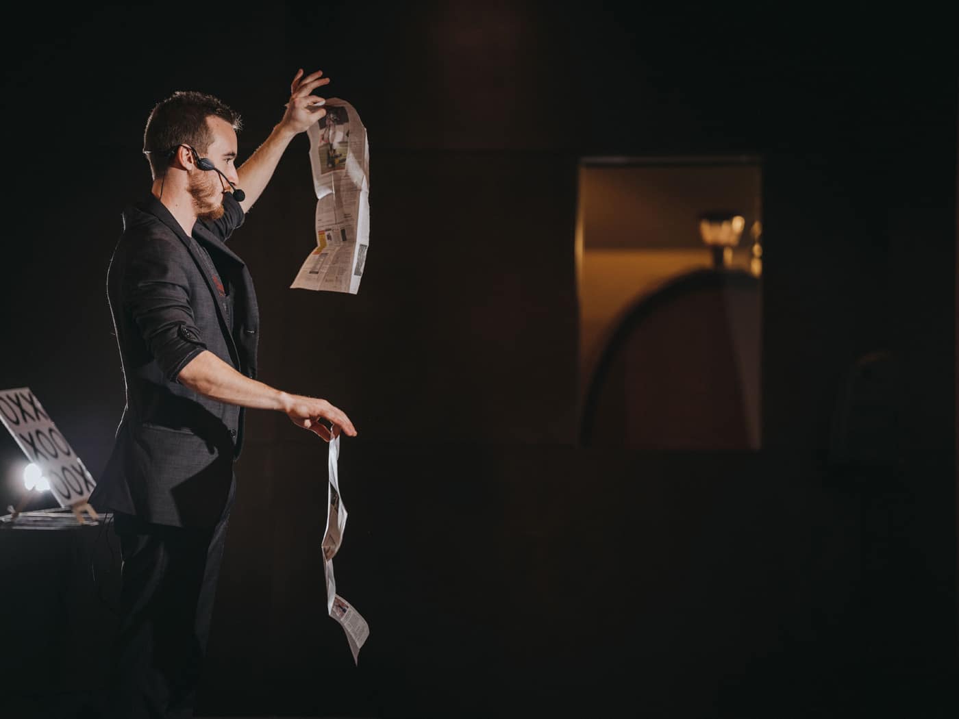 A performer in a dark setting demonstrates a magic trick with seemingly floating pieces of paper.