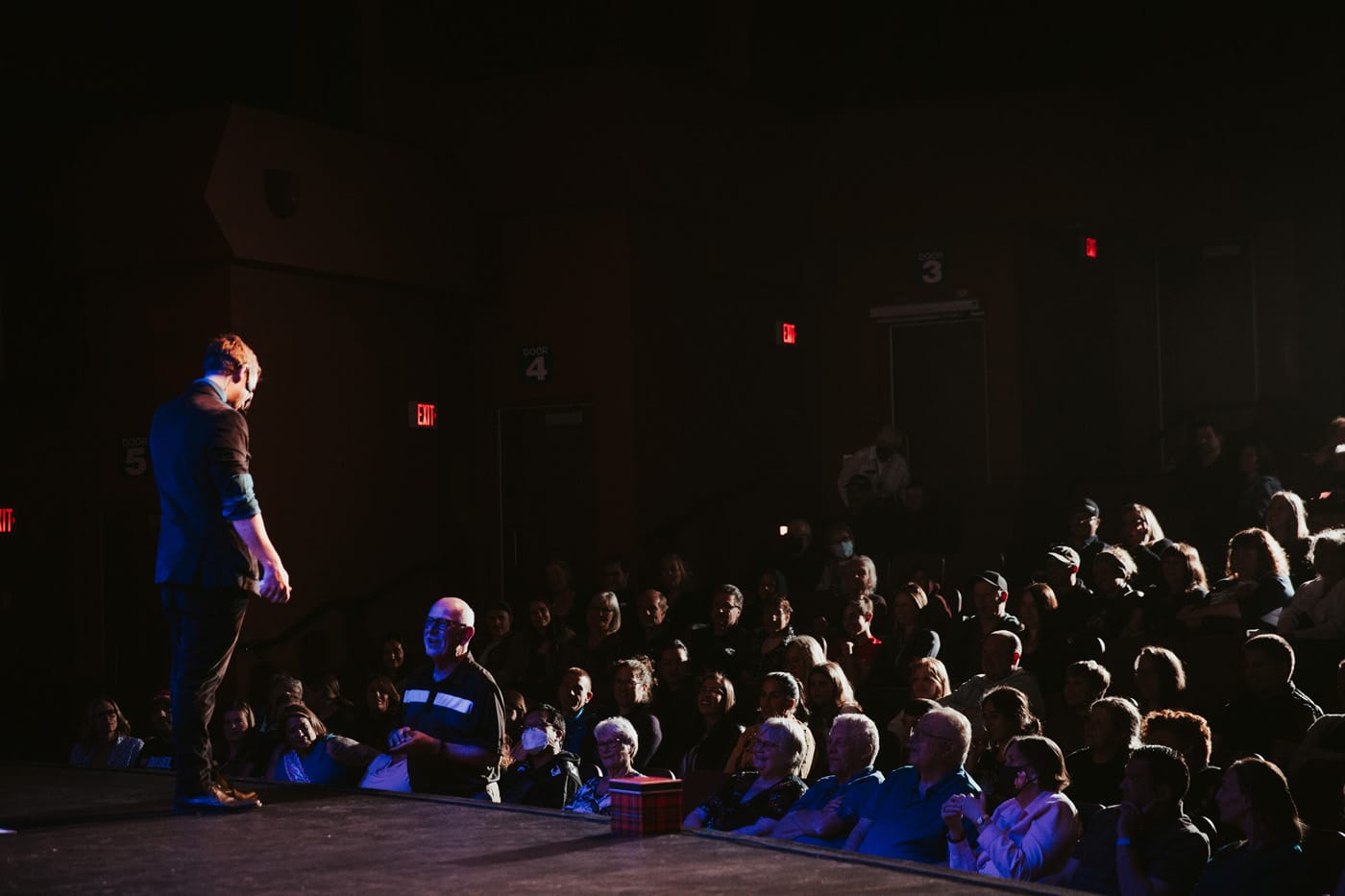A performer on stage interacting with an audience in a theater setting, with a crowd watching attentively.