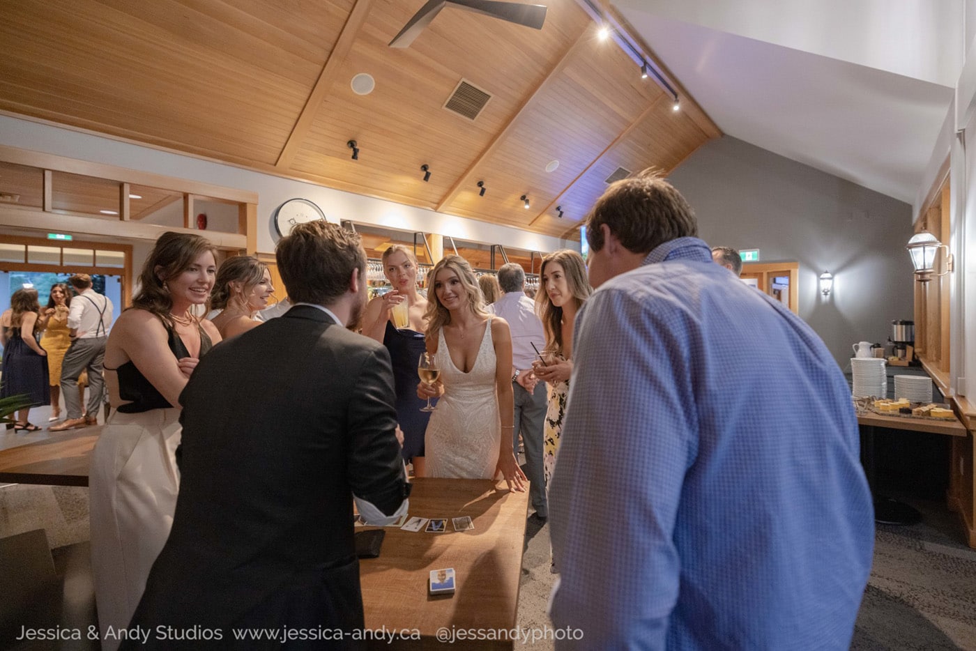 A group of people socialize and enjoy drinks at a stylish indoor venue, featuring wood accents and a well-lit bar area.
