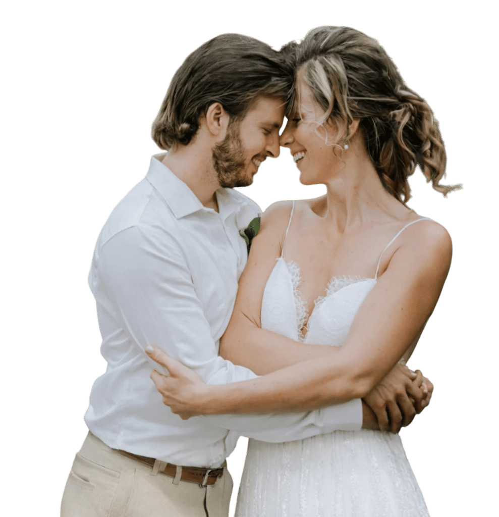 A happy couple embraces, smiling at each other, with the woman wearing a white wedding dress and the man in a white shirt.