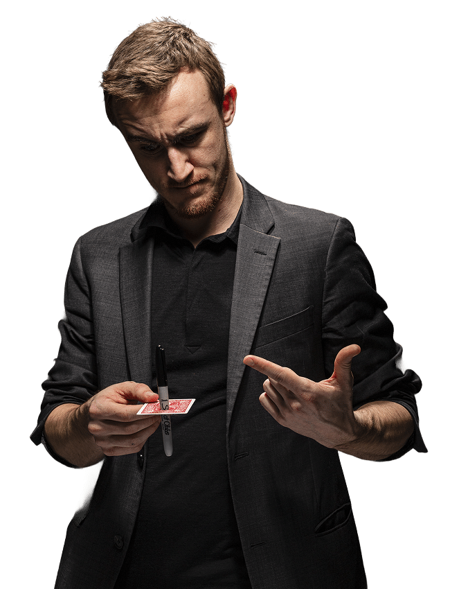 A magician in a black suit holding a playing card with a marker, looking thoughtfully at the card.