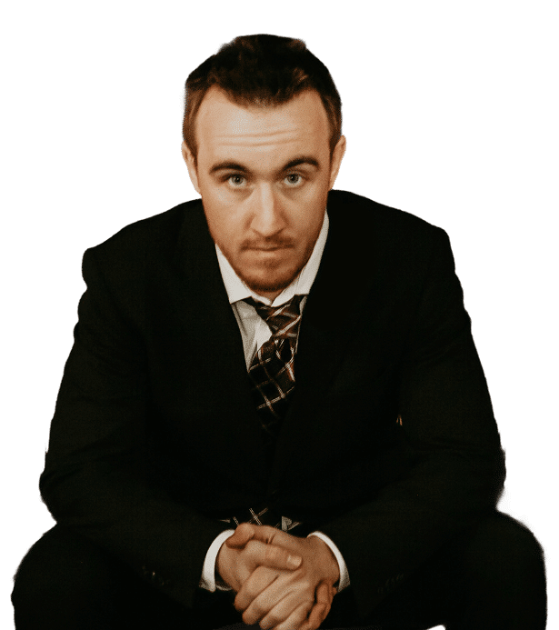 A man in a suit is sitting with his hands clasped, looking directly at the camera with a serious expression.