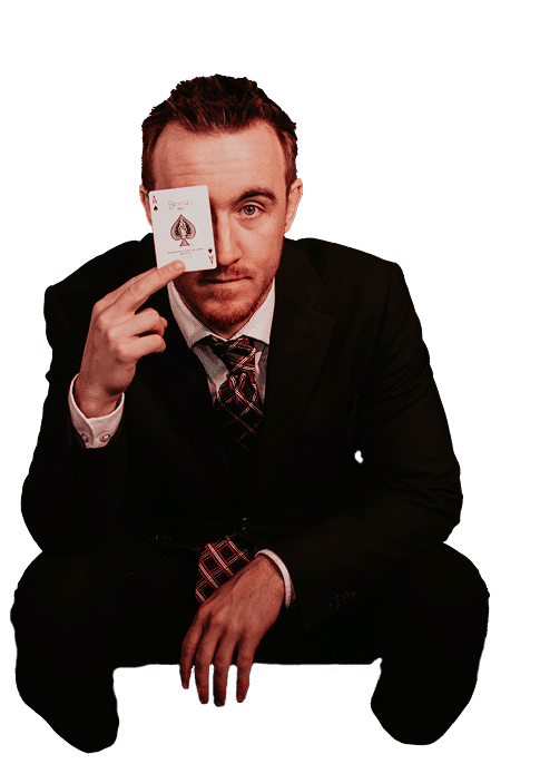 A man in a suit is squatting and holding an ace of spades card in front of his face.
